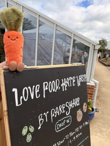 Plushie carrot sat on a sign reading 'Love Food, Hate Waste' by FareShare